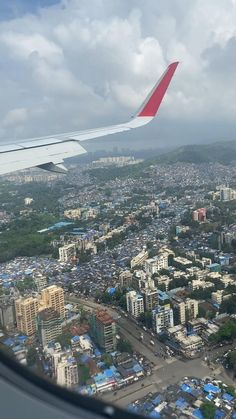 an airplane wing flying over a city with lots of blue buildings and green trees in the foreground