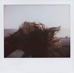 a polaroid photograph of a woman with her hair blowing in the wind, taken from inside a car