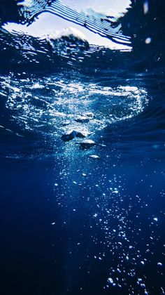 an underwater view of the ocean with sunlight shining on the water and bubbles coming off the surface