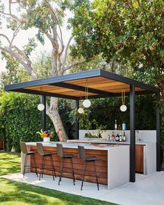 an outdoor bar with stools next to it under a tree and some bushes in the background