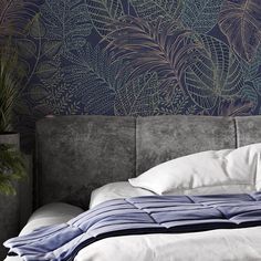 a bed with pillows and blankets in front of a wallpapered headboard that has leaves on it