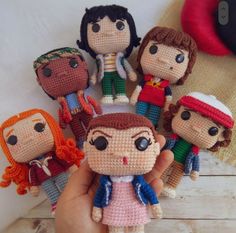 a hand holding a small crocheted doll surrounded by other tiny dolls on a wooden table