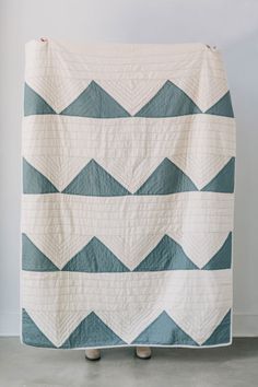 a white and blue quilt is hanging up on a stand in front of a wall