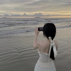 a woman standing on the beach looking at the ocean with her back to the camera