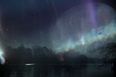 the aurora lights shine brightly in the night sky over a body of water and trees