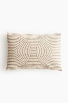 a beige and white striped pillow with circles on the front, sitting against a white wall