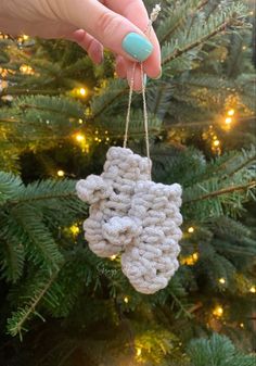 a hand holding a crocheted ornament in front of a christmas tree