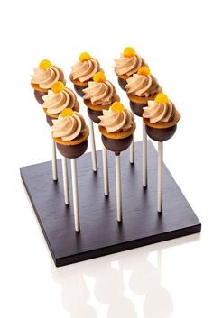 several cupcakes with frosting and orange slices on top are arranged on white sticks