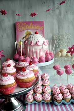 a table topped with lots of cupcakes covered in frosting and pink icing