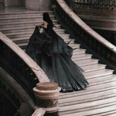 a woman in a black dress walking down some stairs