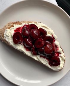 a piece of bread with cream and cherries on it sitting on a white plate