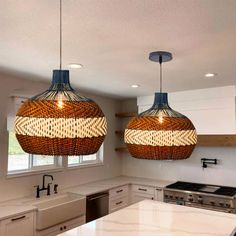 two lights hanging from the ceiling in a kitchen with white counter tops and cabinets below them