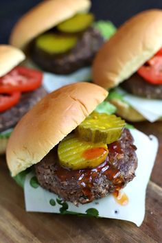 three hamburgers with pickles and tomatoes on them