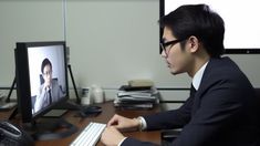 a man sitting at a desk in front of a computer monitor with the image of a woman on it