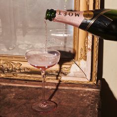 a wine bottle pouring into a glass filled with pink liquid on top of a table