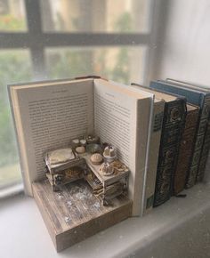 an open book sitting on top of a window sill next to books and cups