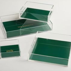 three clear acrylic boxes with green labels on the front and bottom, each containing an individual's name