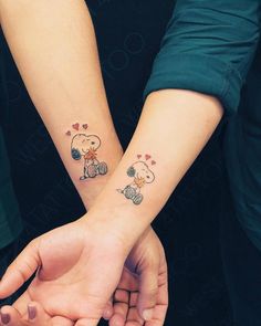 two people holding hands with tattoos on their wrist and one has a small dog in the middle