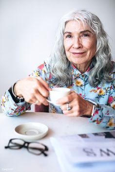 an older woman sitting at a table holding a cup