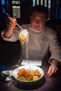 a man in chef's uniform is eating noodles with chopsticks on a plate