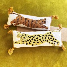 two decorative pillows with animals on them are sitting on a green velvet surface, one has a tiger and the other has a cheetah