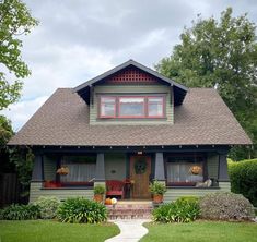 a green house with red trim on the front door and windows, along with landscaping