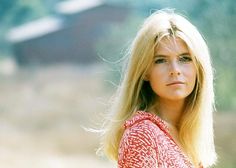 a woman with long blonde hair standing in front of a field and looking off into the distance