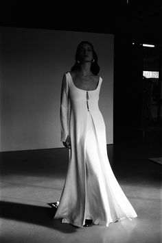 a black and white photo of a woman in a long dress standing with her hands on her hips