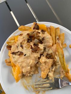 a white plate topped with french fries covered in gravy next to a fork