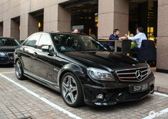 a black car parked in front of a building with people sitting at tables outside it