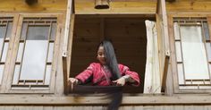 a woman with long black hair standing in an open window