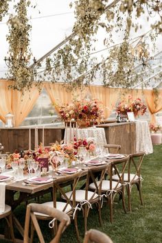 a table set up for an outdoor wedding with flowers and greenery on the tables