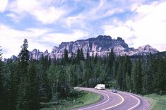 a truck is driving down the road in front of some trees and mountains with a sky background