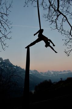 a person is performing aerial acrobatics on a pole in front of mountains