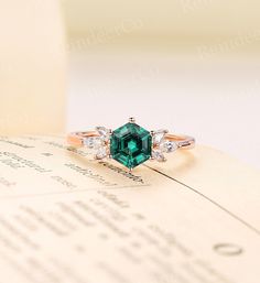 an emerald and diamond ring sitting on top of a piece of paper next to a book