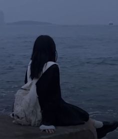 a woman sitting on the edge of a cliff looking out at the ocean in the rain