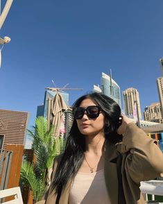 a woman wearing sunglasses standing in front of a cityscape with tall buildings behind her