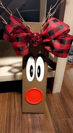 a brown paper bag with a red nose and plaid bow on the top, sitting on a wood floor