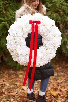 a woman holding a white wreath with red ribbon