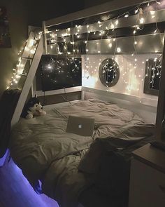 a bed room with a laptop on top of it and lights strung from the ceiling