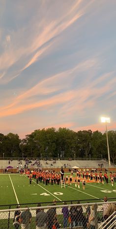 a group of people standing on top of a field next to a soccer field at sunset