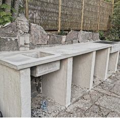 an outdoor concrete bench with two sinks in the middle and several rocks on the ground