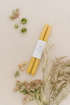 two yellow candles sitting next to some dried flowers