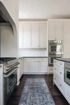 a kitchen with white cabinets and an area rug in front of the stove top oven