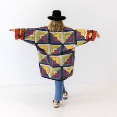 a woman with her arms outstretched wearing a multicolored crocheted coat and hat