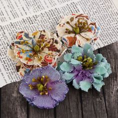 three fabric flowers sitting on top of an open book