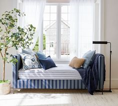 a blue and white striped daybed with pillows on it in front of a window