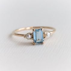 a gold ring with an aqua blue topazte and pearls on the side, sitting on a white surface