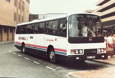 a white bus is parked on the side of the road with people standing around it