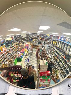 the reflection of two people standing in front of a store filled with shelves full of liquor